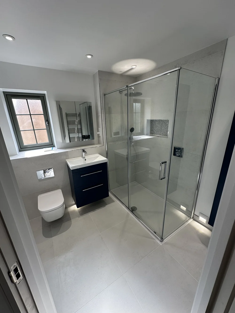 Fitted ensuite with navy vanity, wall-hung WC and corner shower enclosure — bathroom installation Woking